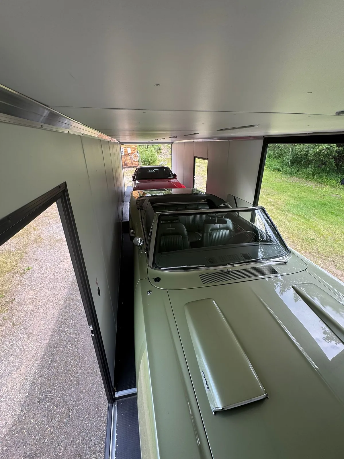 Green classic convertible secured inside an enclosed multi-car trailer.