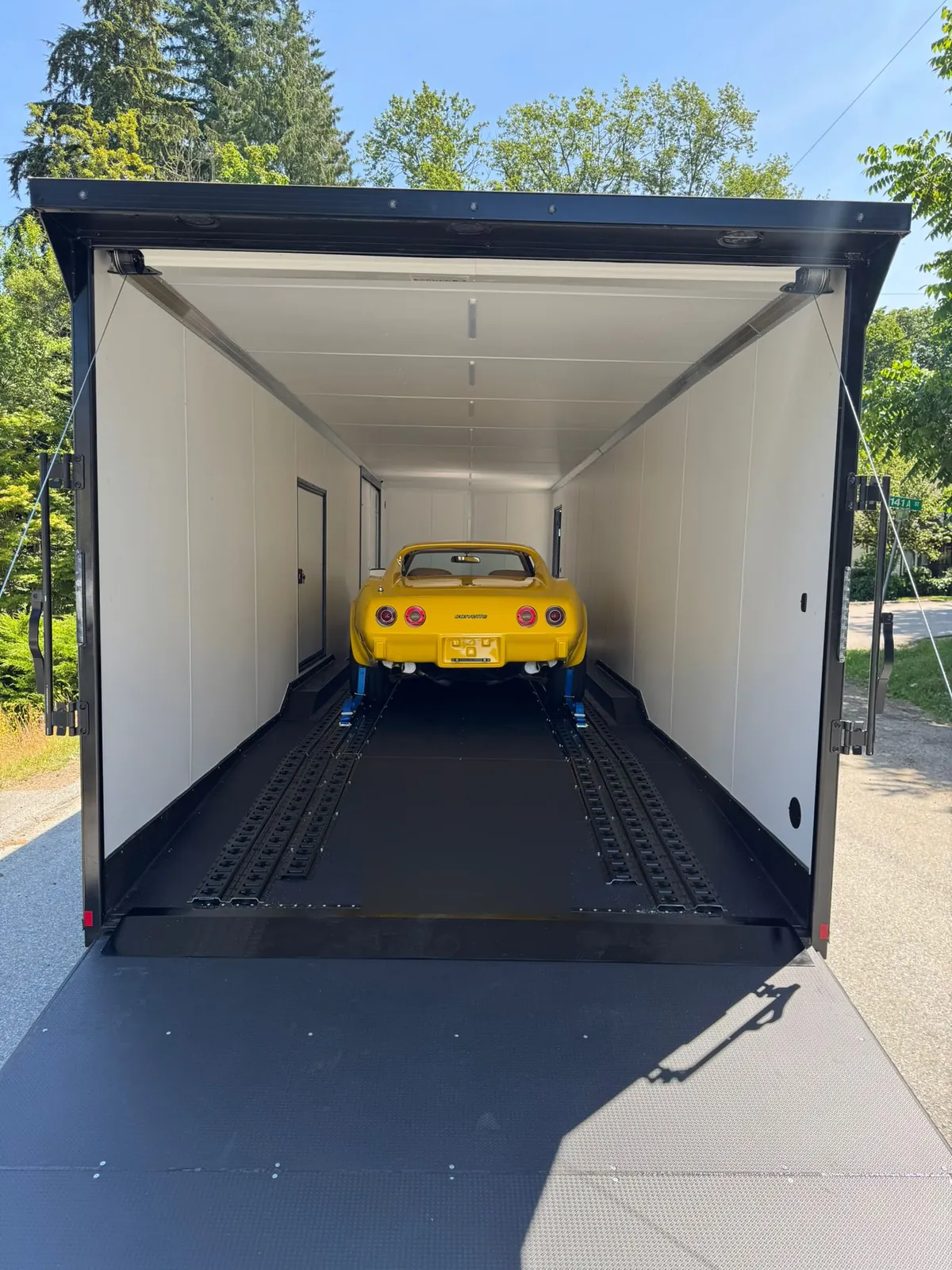Yellow Chevrolet Corvette C3 loaded inside an enclosed trailer with the ramp down.