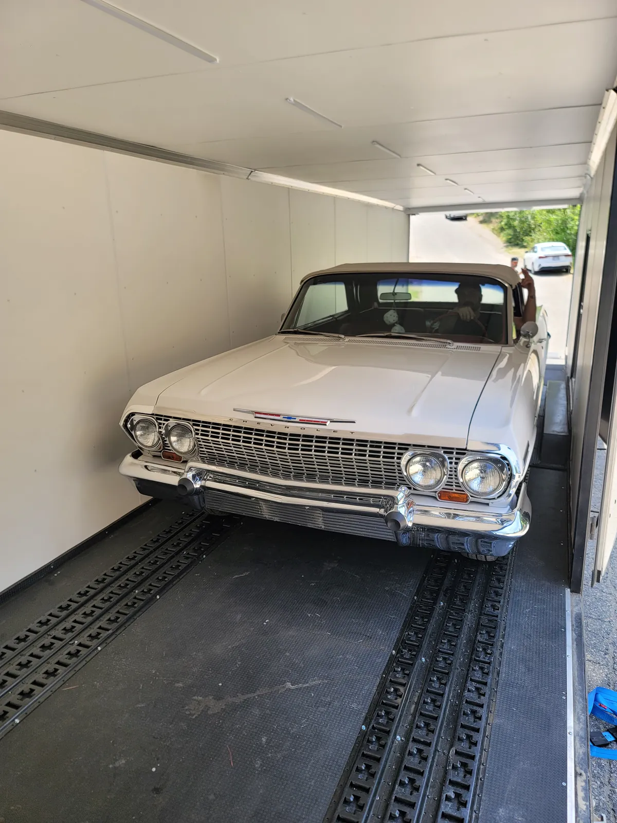 White 1963 Chevrolet Impala loaded inside an enclosed transport trailer.
