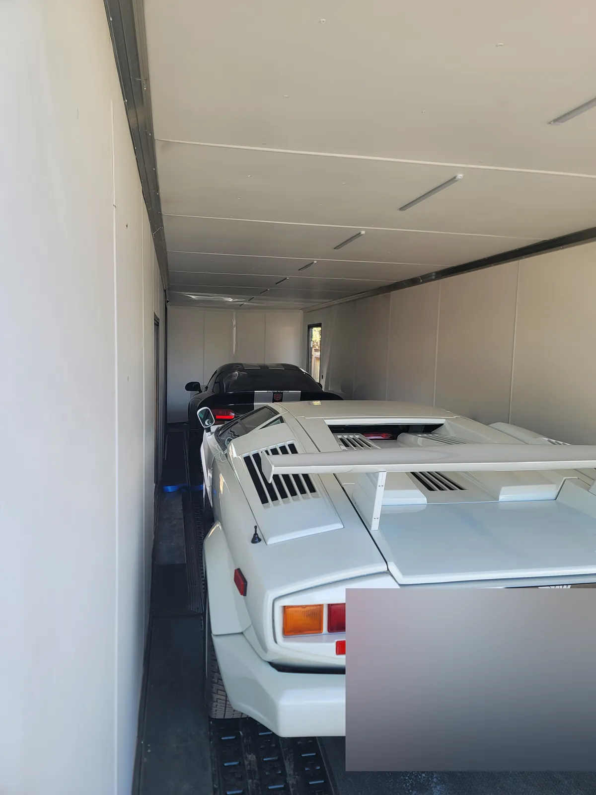 White Lamborghini Countach loaded inside an enclosed multi-car transport trailer.