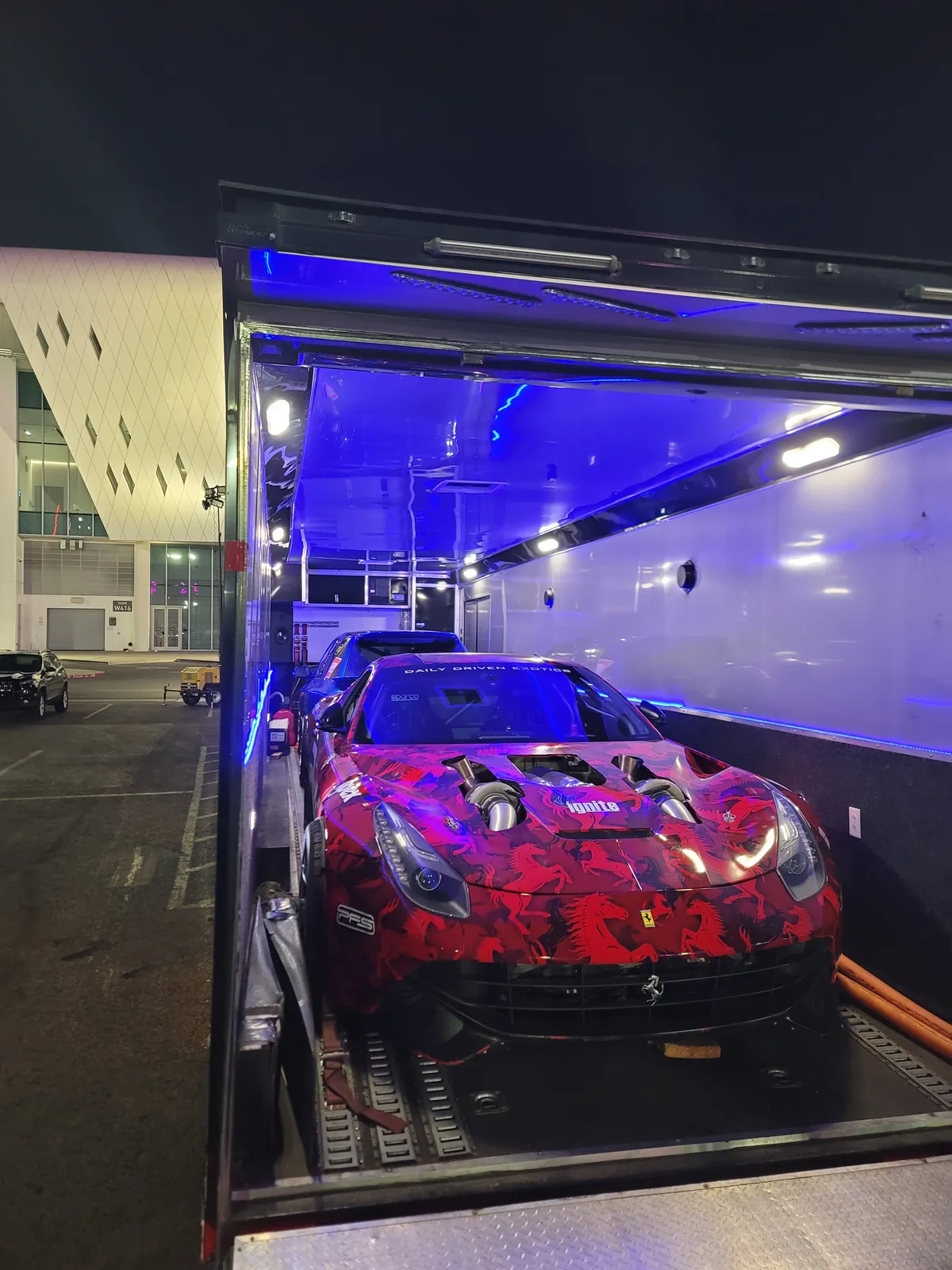 Camouflage-wrapped Ferrari loaded inside an enclosed trailer at night.