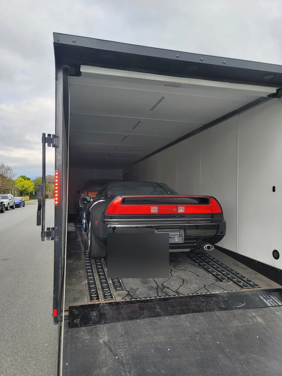 Black Acura NSX loaded inside an enclosed trailer with the ramp down.