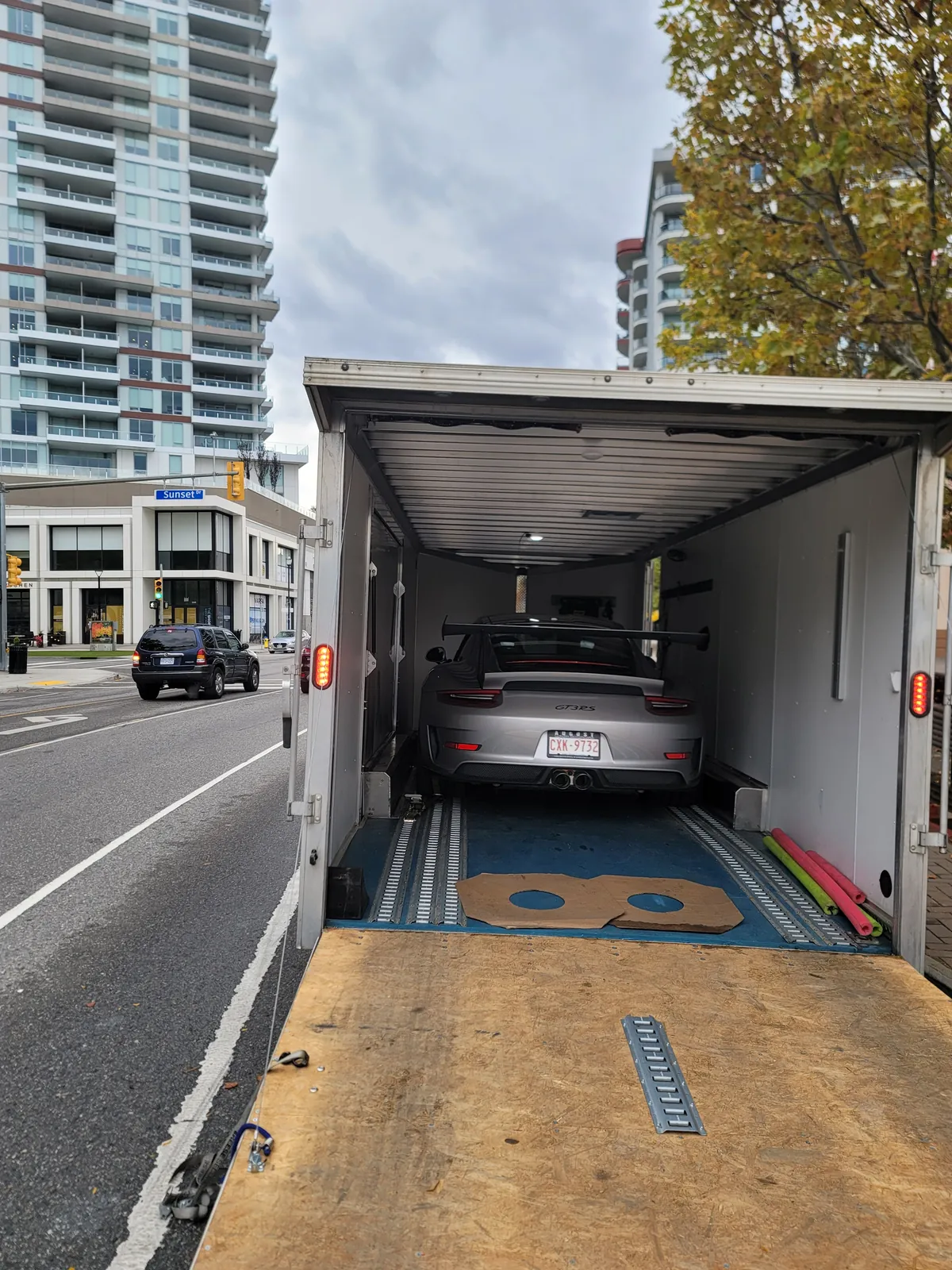 Porsche GT3 RS being loaded up the ramp into an enclosed trailer on a city street.