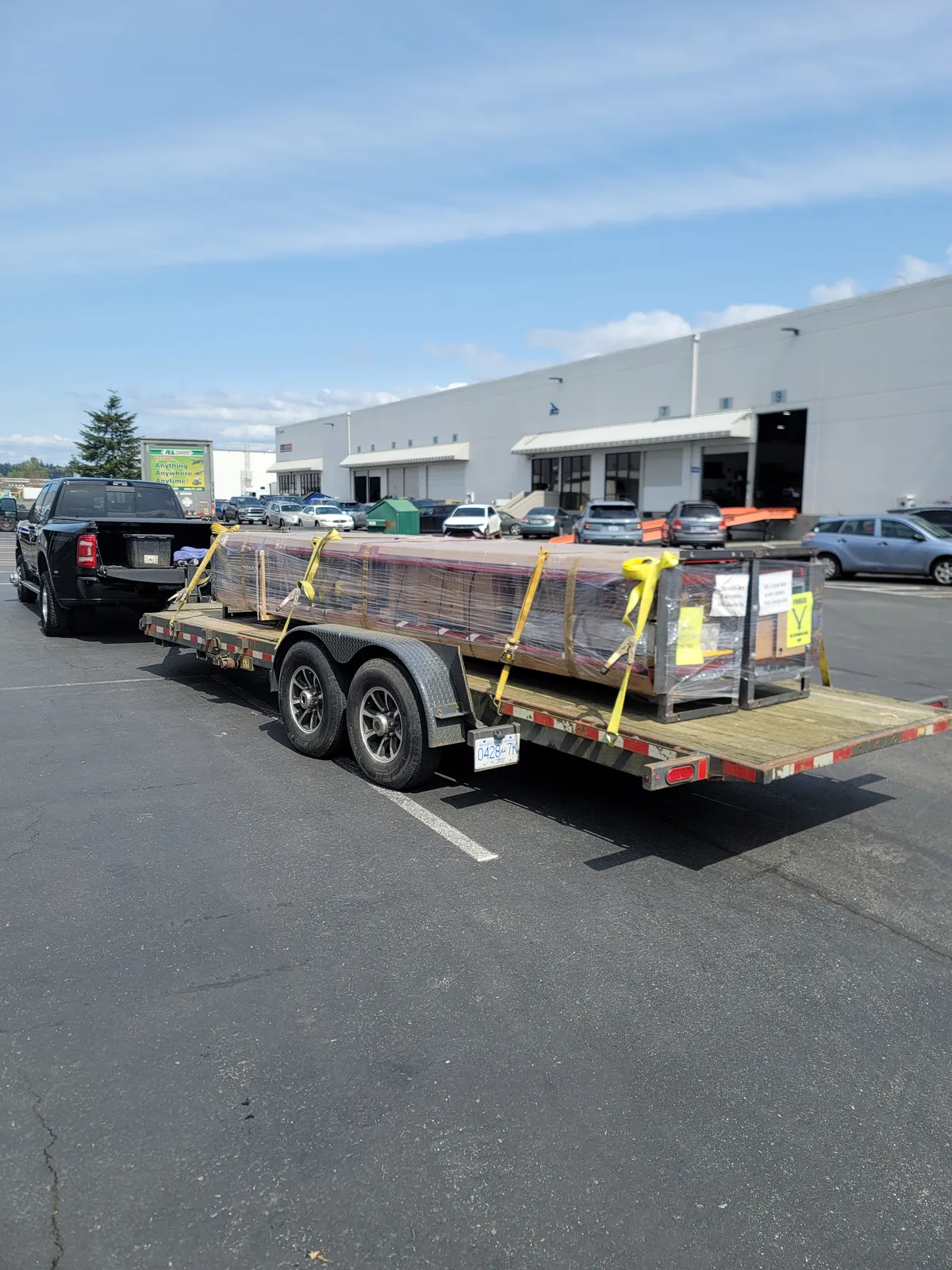 Flatbed trailer with strapped freight loaded behind a pickup truck.