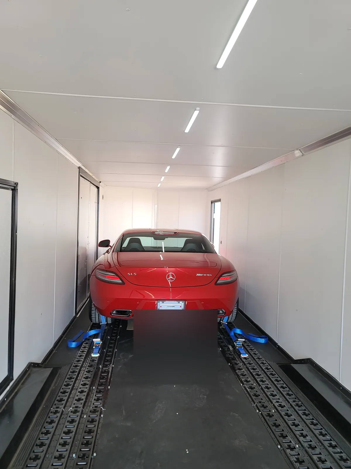 Red Mercedes-Benz SLS AMG secured inside a clean enclosed trailer interior.